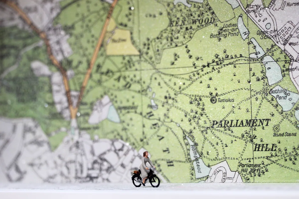 Close-up of a Glass Cathedral box: a tiny cyclist rides past an old map of Hampstead Heath, Parliament Hill marked behind her.