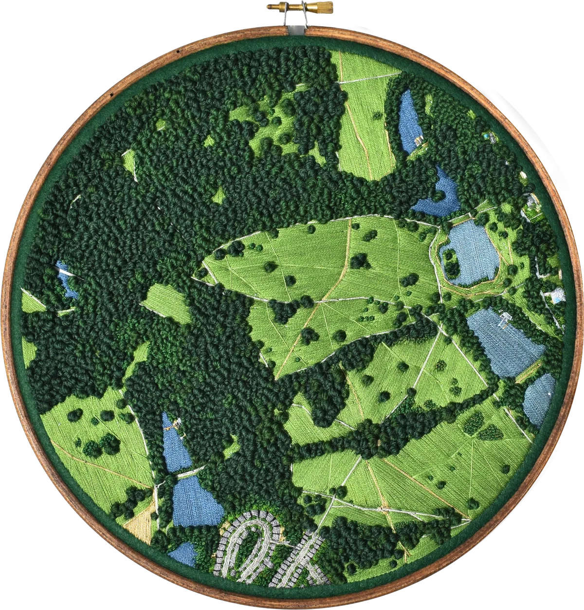 Round embroidery in a wooden hoop: an aerial view of the Heath stitched in greens and blues, with dense knotted woodland, pale meadows, ponds and a curve of houses.