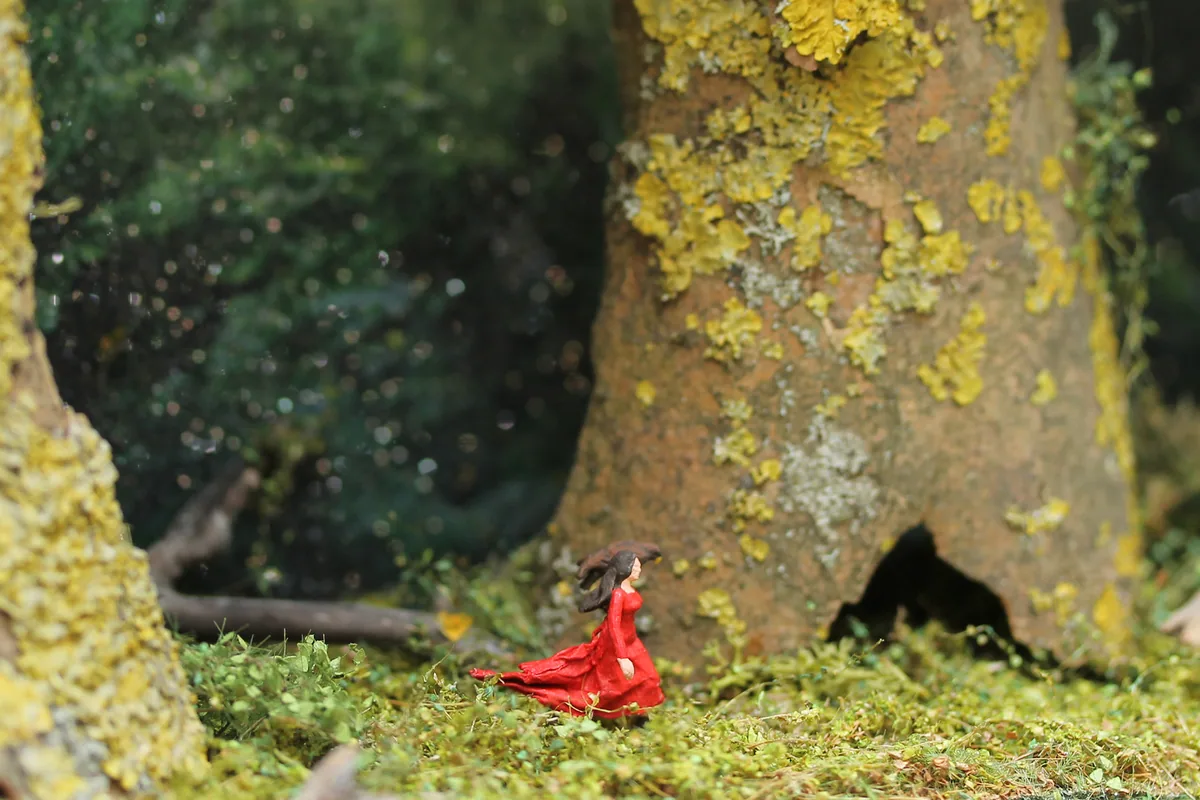 Closer detail: the figure in red beside a hollow tree trunk.