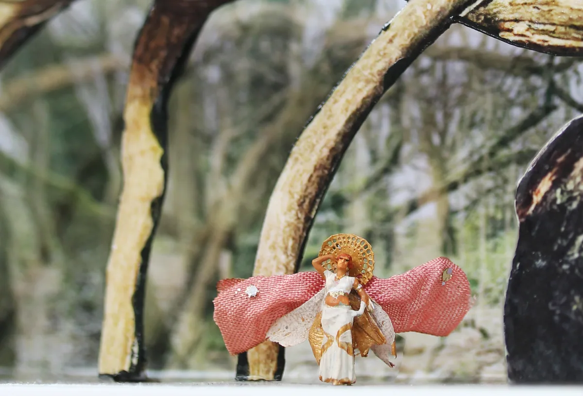 Detail: the tiny heroine in her moth-wing costume beneath arching branches.