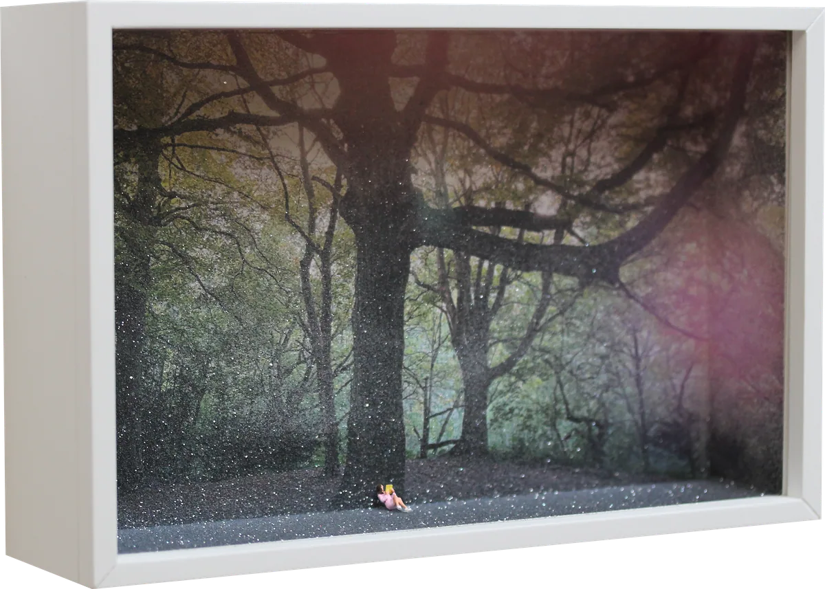 Glass Cathedral box diorama: a tiny figure in pink sits reading at the foot of a great tree in a misty, sparkling wood.