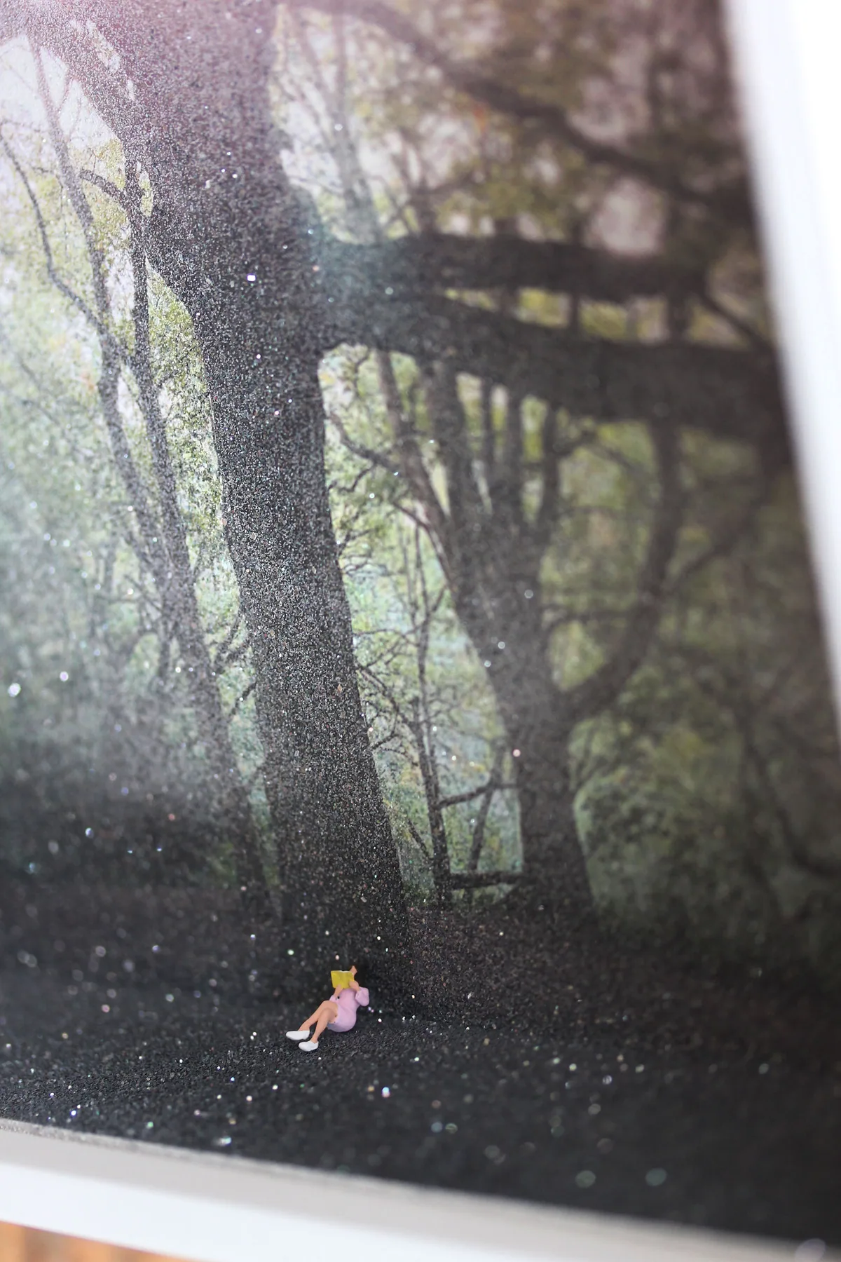 Detail: the tiny reader with her book, sitting on the sparkling ground at the foot of the tree.