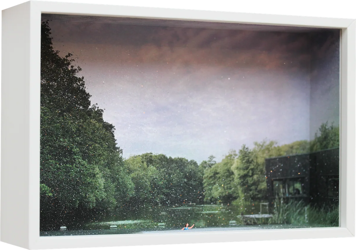 Glass Cathedral box diorama: a tiny swimmer in a Heath pond, surrounded by trees beneath a soft pink sky, with a bathing hut on the right.