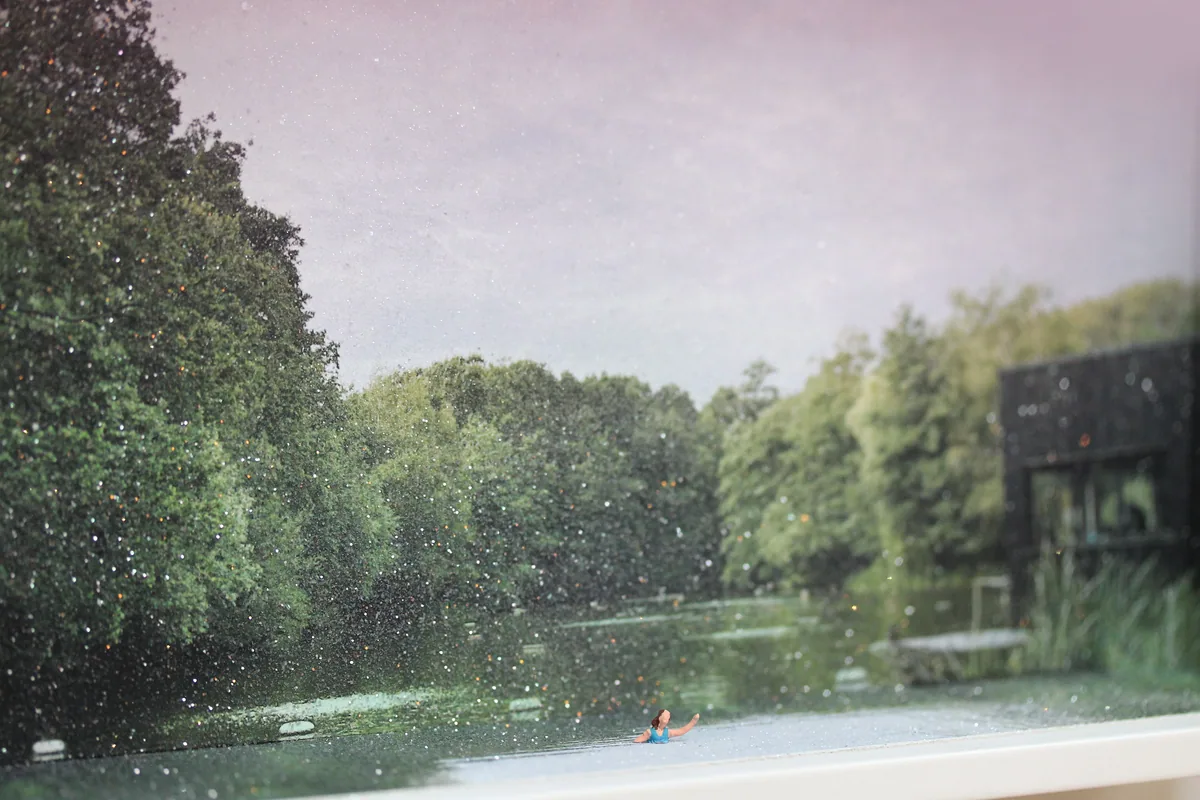 Detail: the swimmer in the sparkling water, with the trees and bathing hut behind.